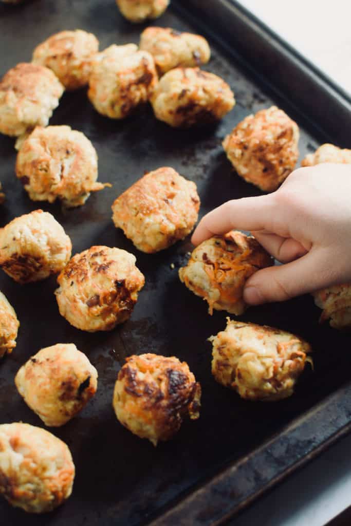 child hand grabbing chicken meatball off black pan