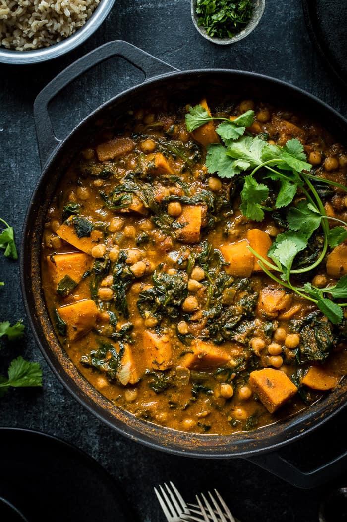 Close up of a black pan of vegan chickpea, sweet potato and spinach curry topped with fresh coriander.