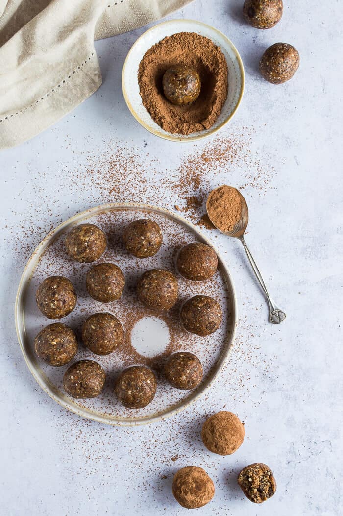 Vegan chocolate chip peanut butter energy balls dusted with cacao powder on a white plate on a grey background.