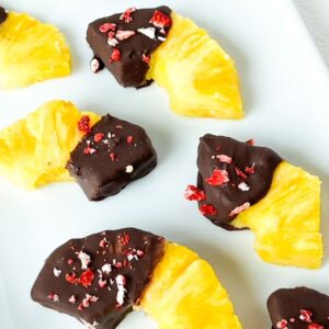 Thirds and halves of pineapple rings with one end covered in chocolate and topped with crushed freeze dried strawberries.