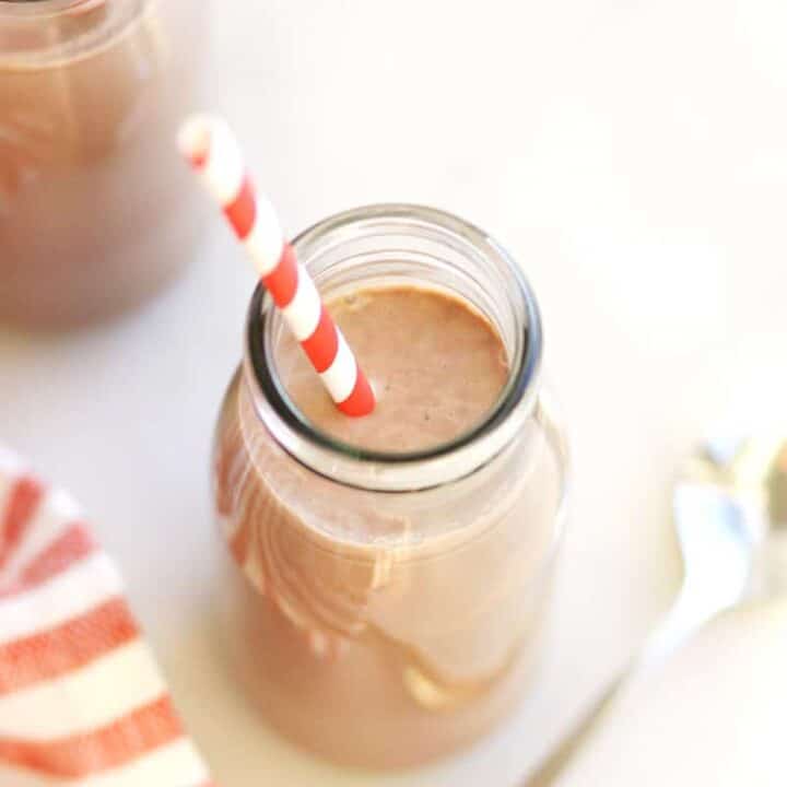 a milk bottle of frothy chocolate milk with a spoon next to it and a red and white striped towel