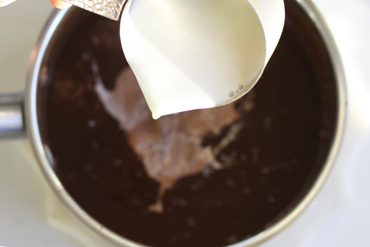 a cup of milk being pured into a saucepan of chocolate