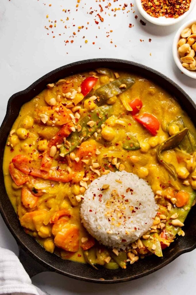 Overhead view of cast iron pan with a yellow curry with chickpeas and vegetables and a round pat of white rice.