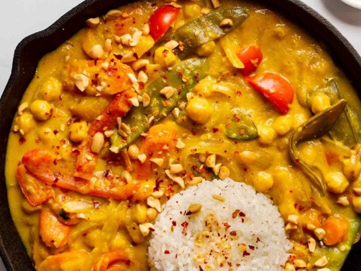 Overhead view of cast iron pan with a yellow curry with chickpeas and vegetables and a round pat of white rice.