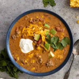 Overhead view of a bowl of creamy taco soup garnished with sour cream, avocado, cilantro, and grated cheddar.