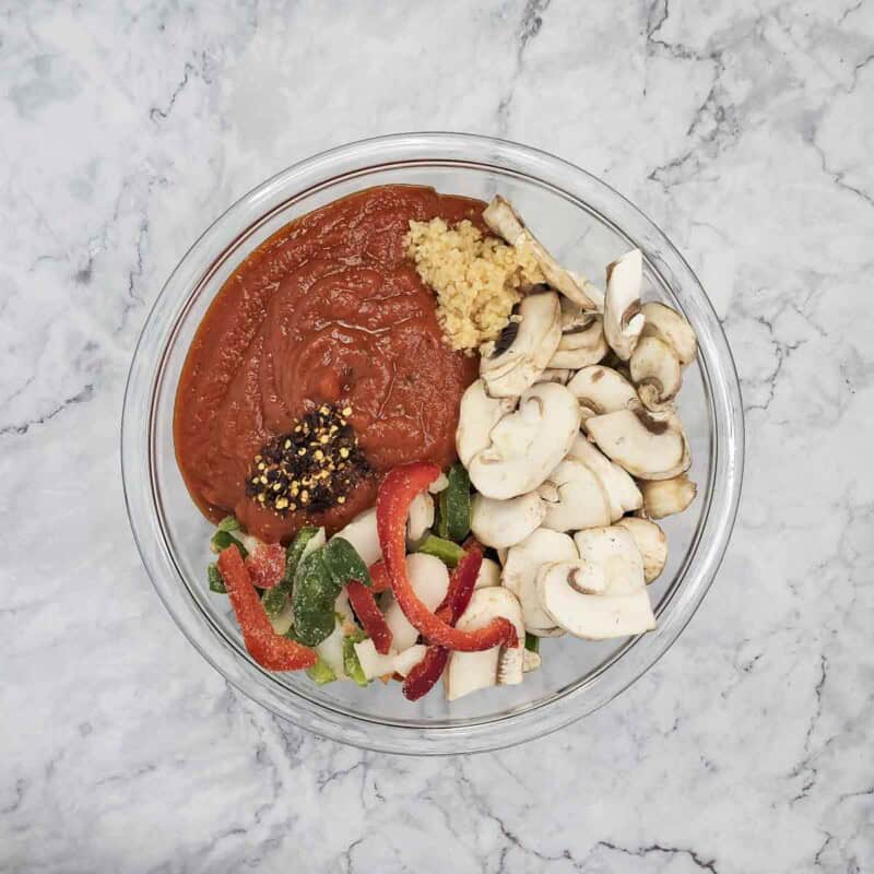 Overhead view of process shot 1 - in a large bowl, combine the marinara, frozen peppers and onions, mushrooms, garlic, and red pepper flakes.