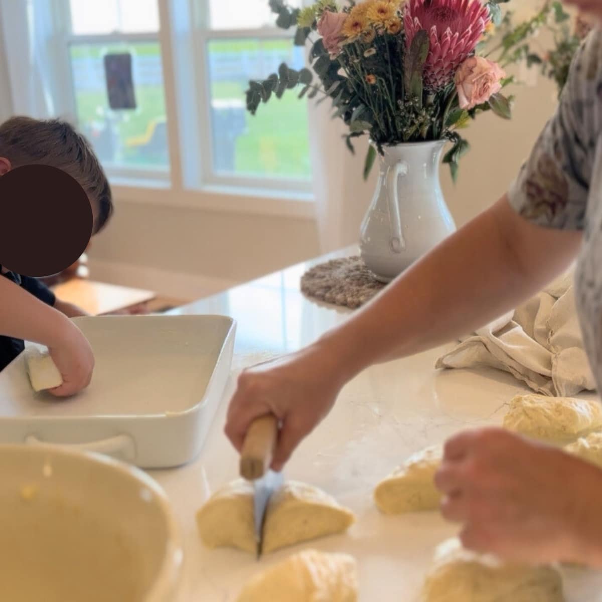 cutting dough into rolls with a bench scraper and buttering baking dish