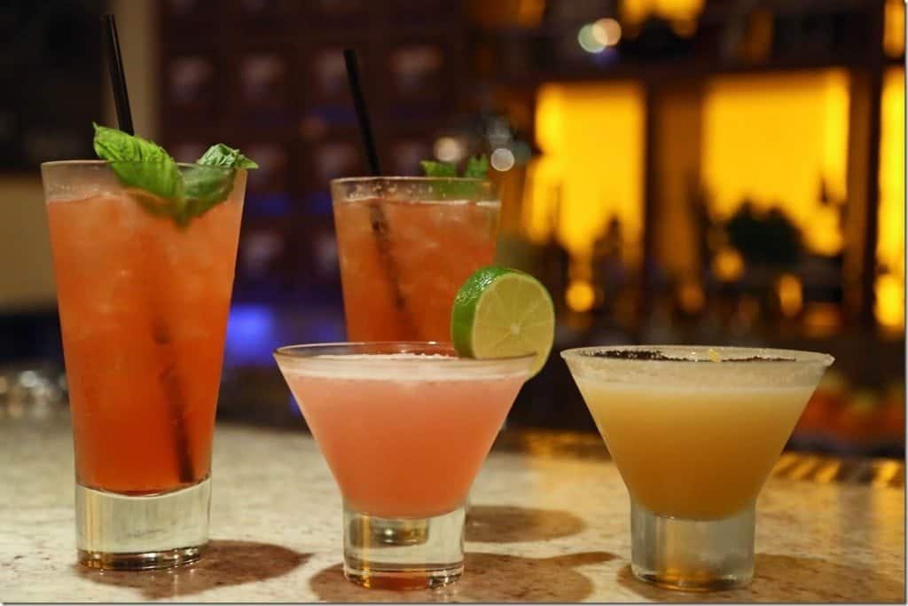 Four Alchemy Bar cocktails on a counter with lights behind them