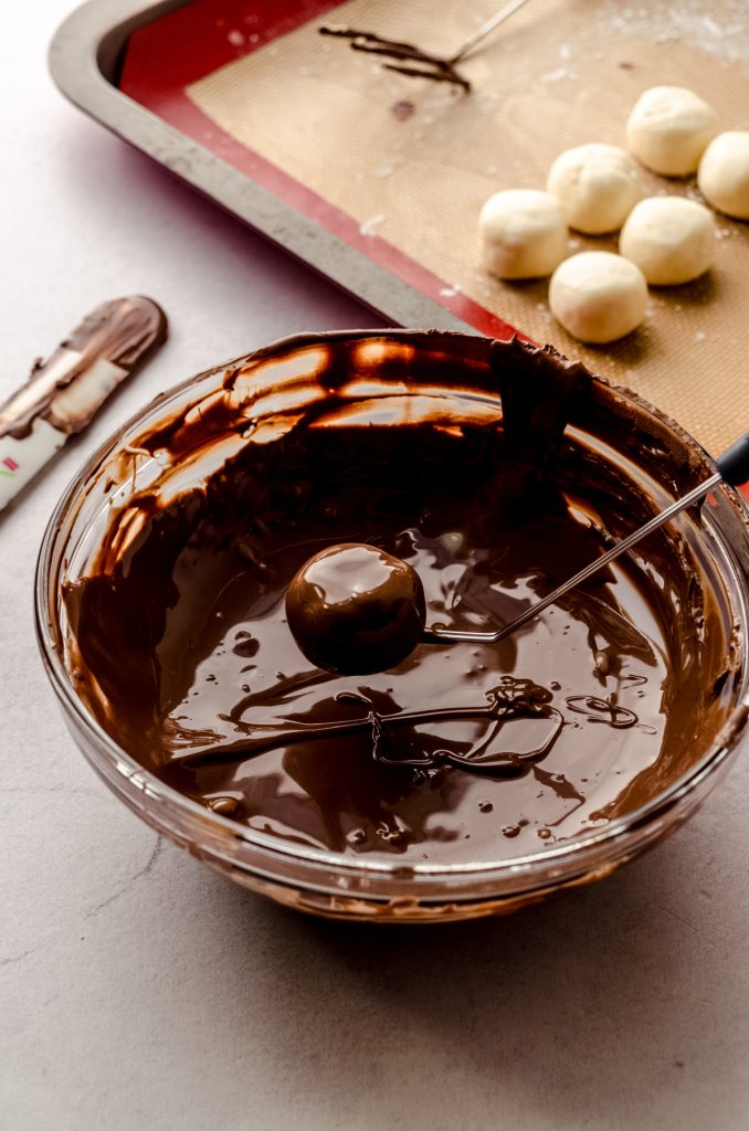 Someone is dipping a buttercream round into chocolate coating to make Easter candy.