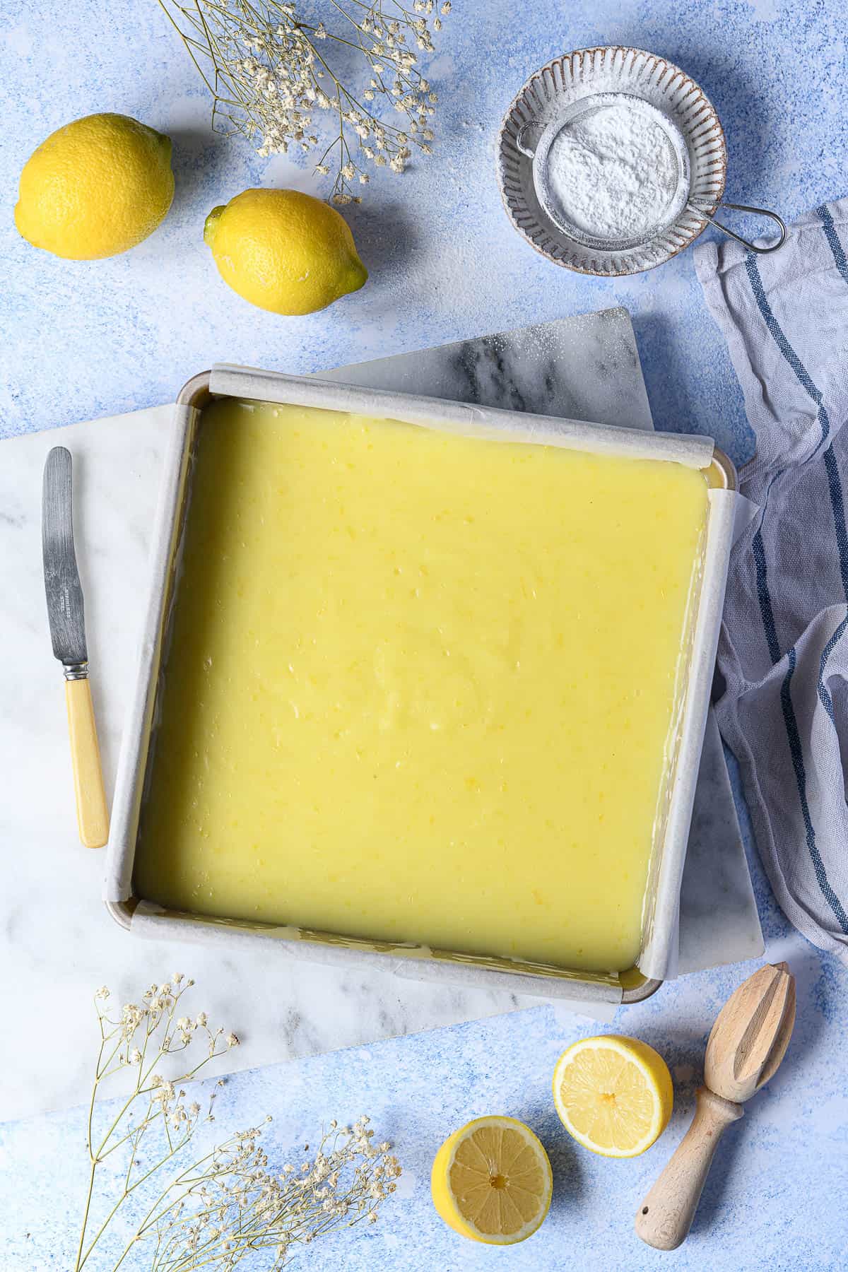 The unsliced lemon bars in a metal cake tin.