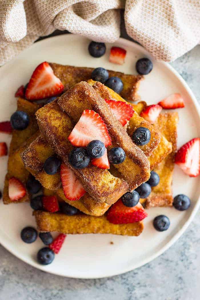 overhead shot of fried french toast sticks on a white plate with fresh berries scattered. 