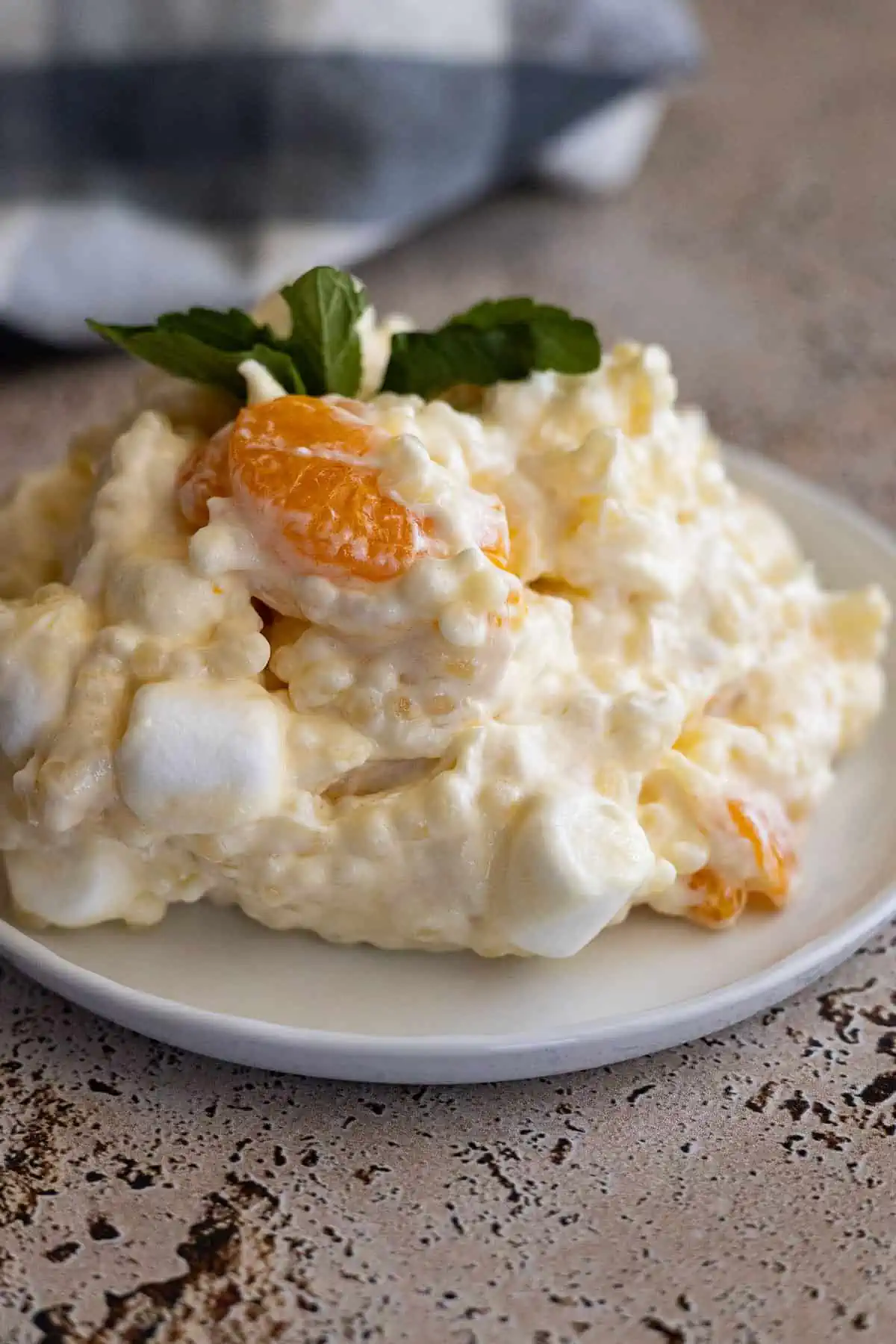 Frog eye salad on a white plate with a blue napkin in the corner. Salad garnished with mint. 