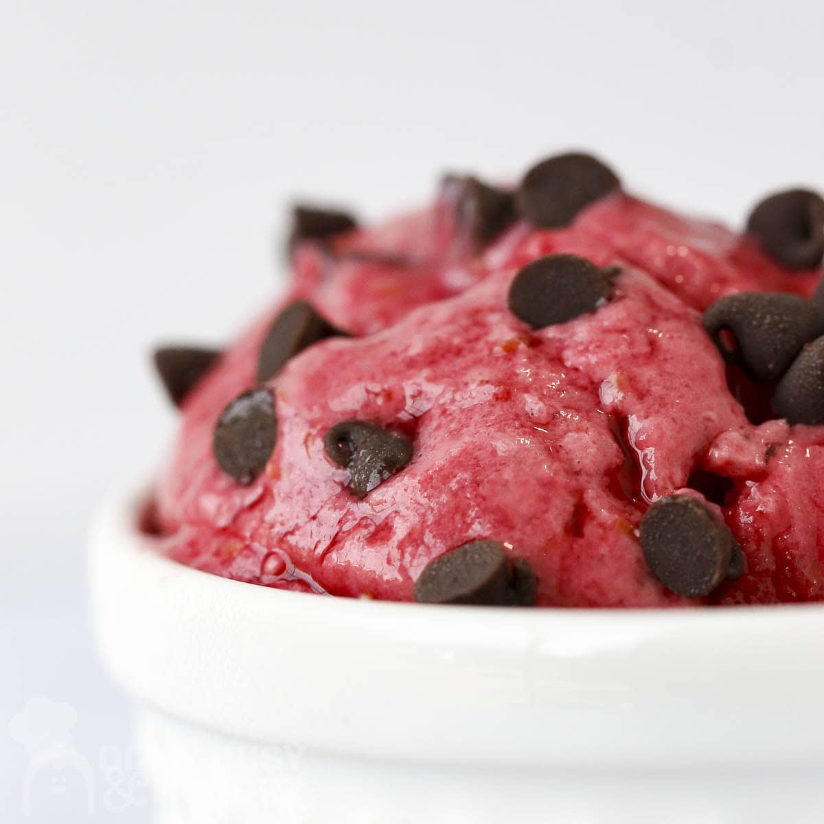 Side shot of raspberry frozen yogut with chocolate chips in a white bowl.