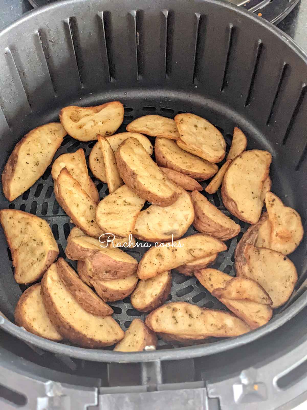 Air fried golden potato wedges in air fryer basket.