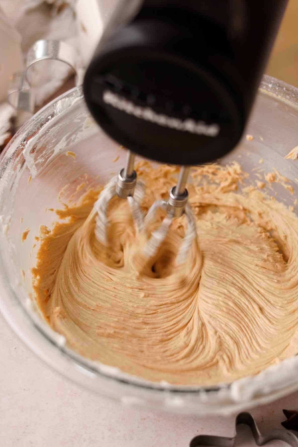 beating gingerbread cream cheese frosting with an electric mixer in a glass bowl