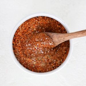 Homemade taco seasoning in a small white bowl with a wooden spoon.