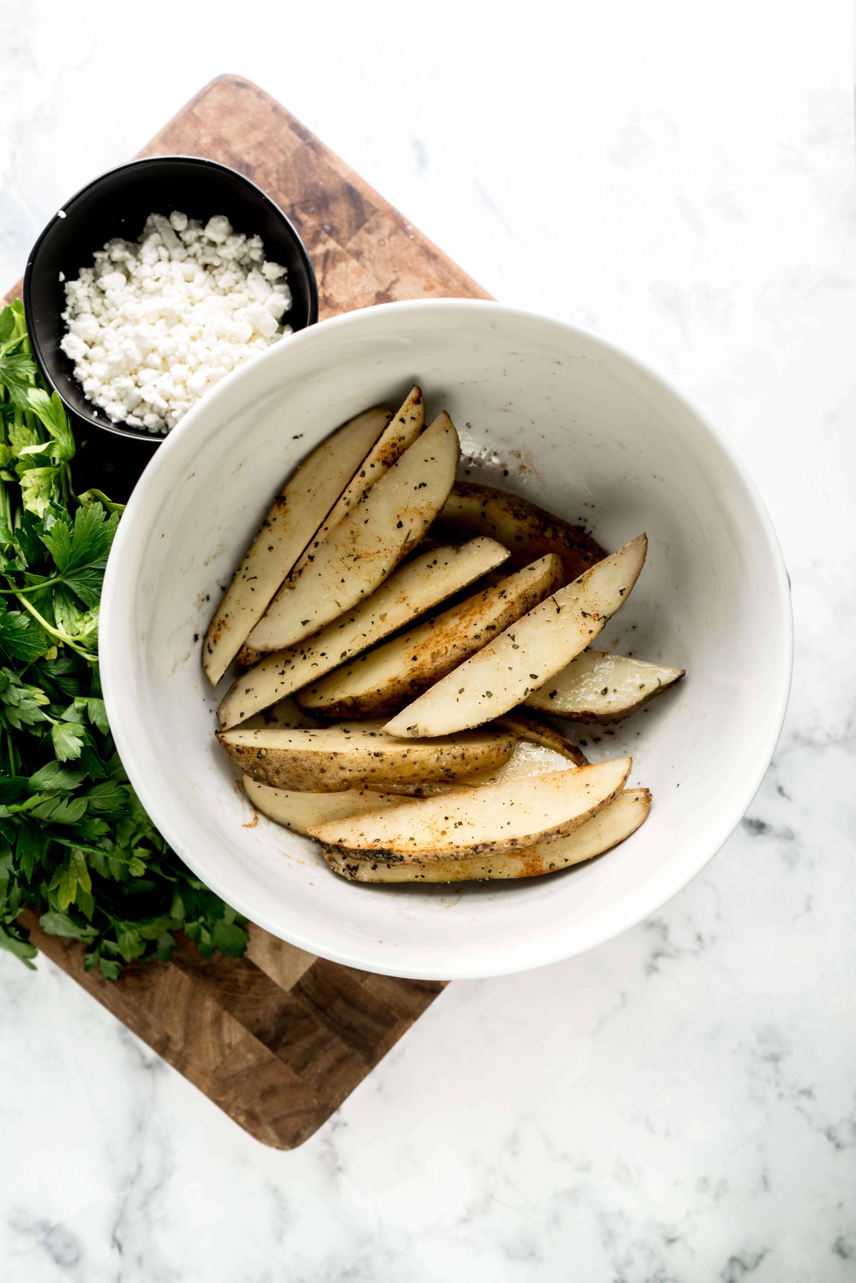 seasoned potato wedges in bowl on cutting board