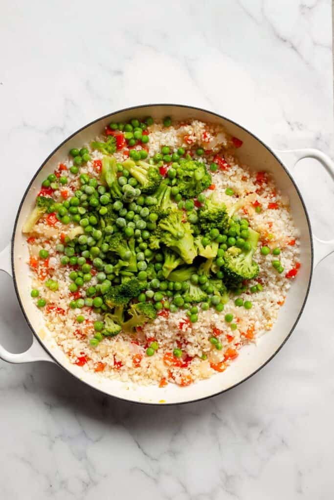 adding cauliflower rice, broccoli, and peas