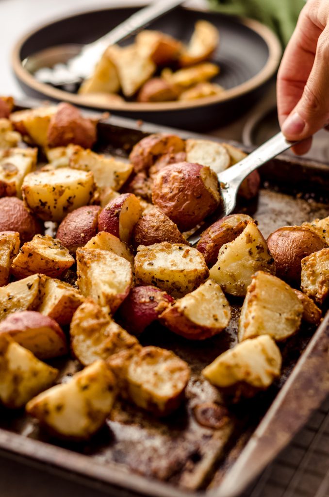 spatula scooping up herbed potatoes from a baking sheet