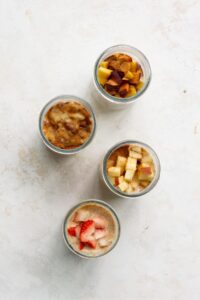 Adding toppings to protein overnight oats base. Four total jars with flavors including: pb&J, peaches and cream, apple pie, and banana bread