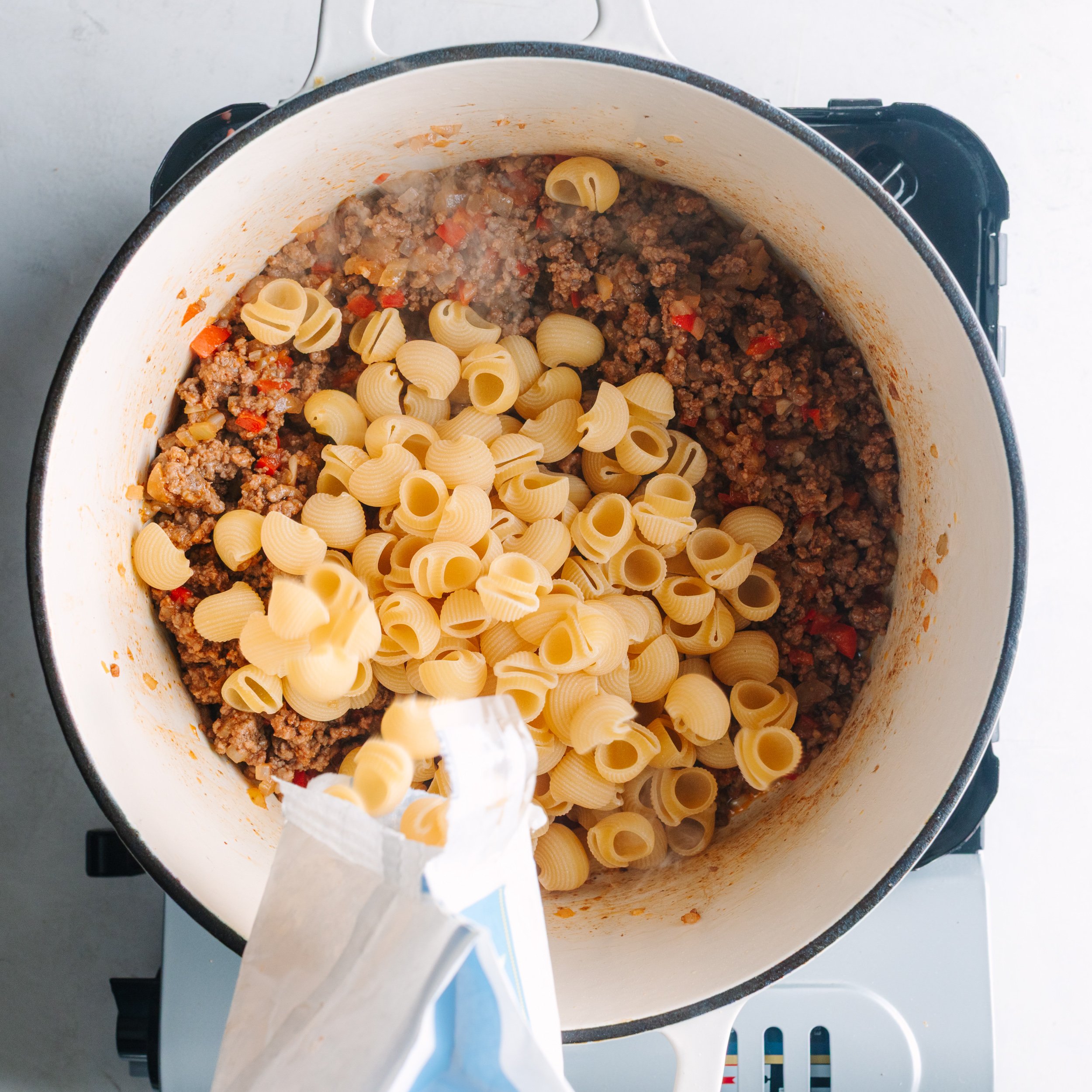 Adding pasta to pot of ground beef, spices, and vegetables. 