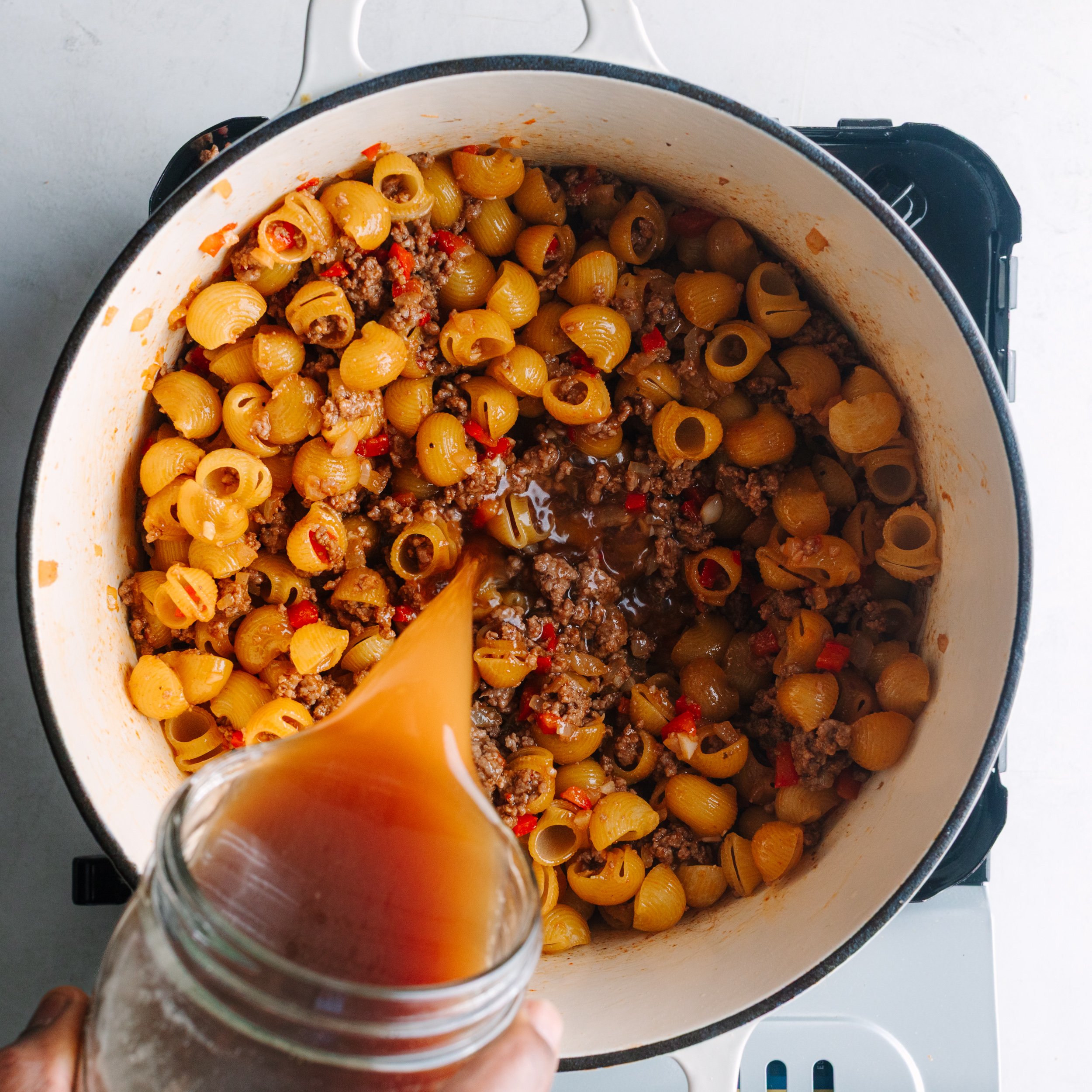Pouring beef broth into pot with pasta and meat sauce