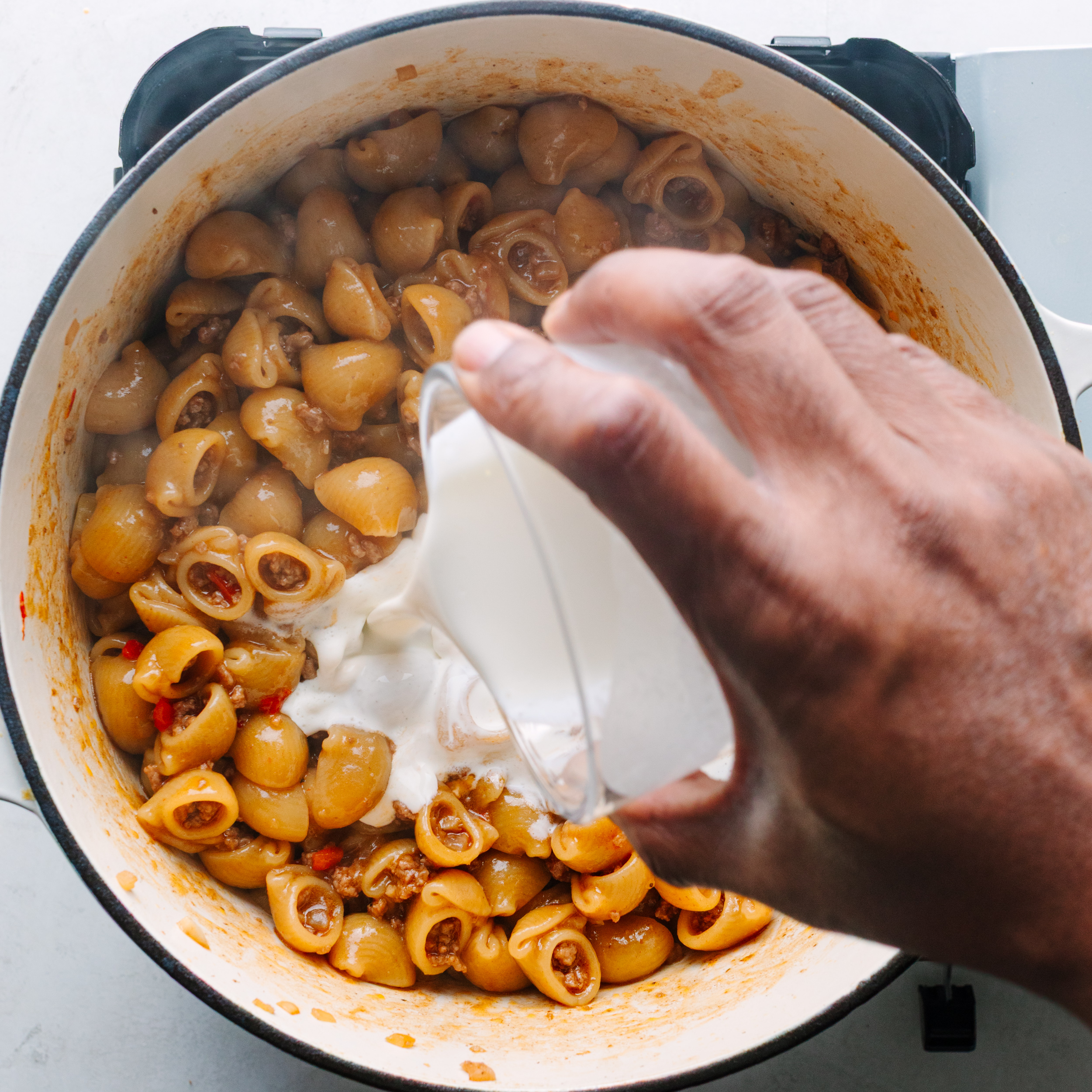 Pouring heavy cream into pasta mix. 