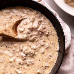 A black cast iron pan with a sausage gravy and wooden spoon