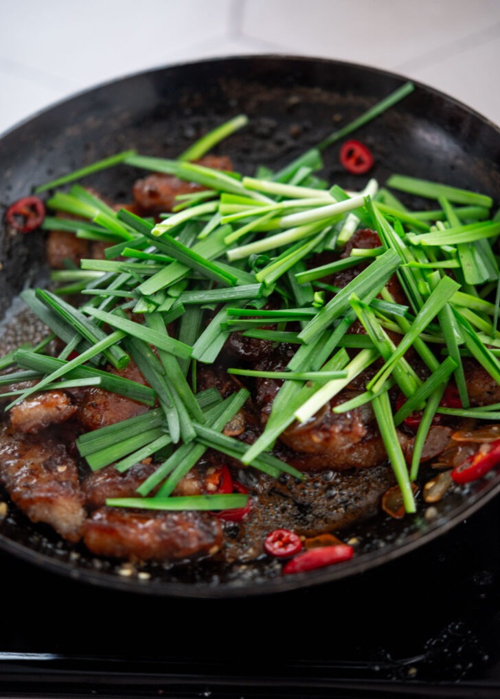 Fresh chives being added to honey garlic pork in the final cooking step