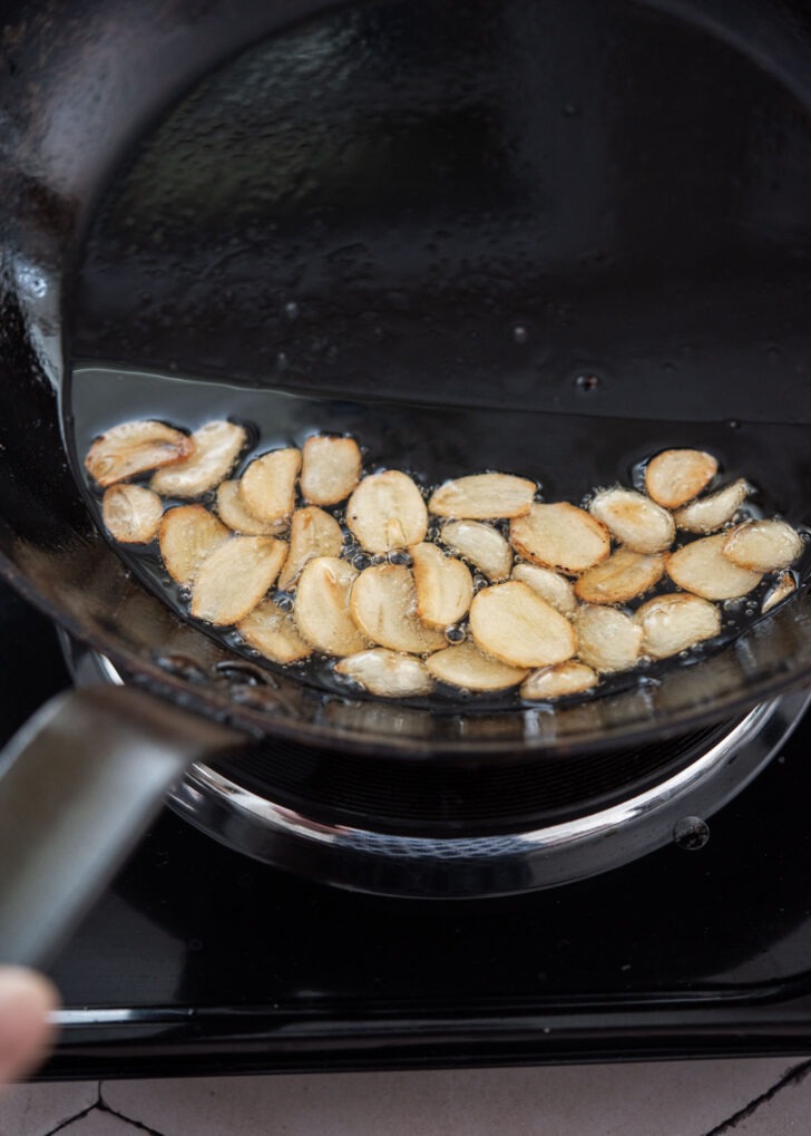 Garlic slices browning and crisping in hot oil in a skillet
