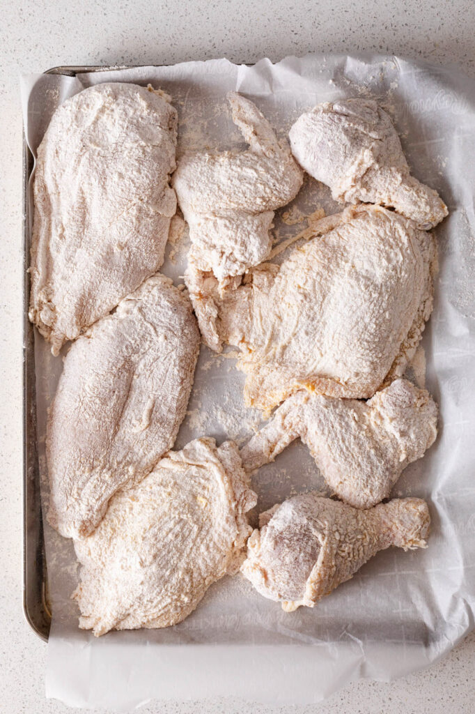 floured chicken on a parchment lined sheet pan