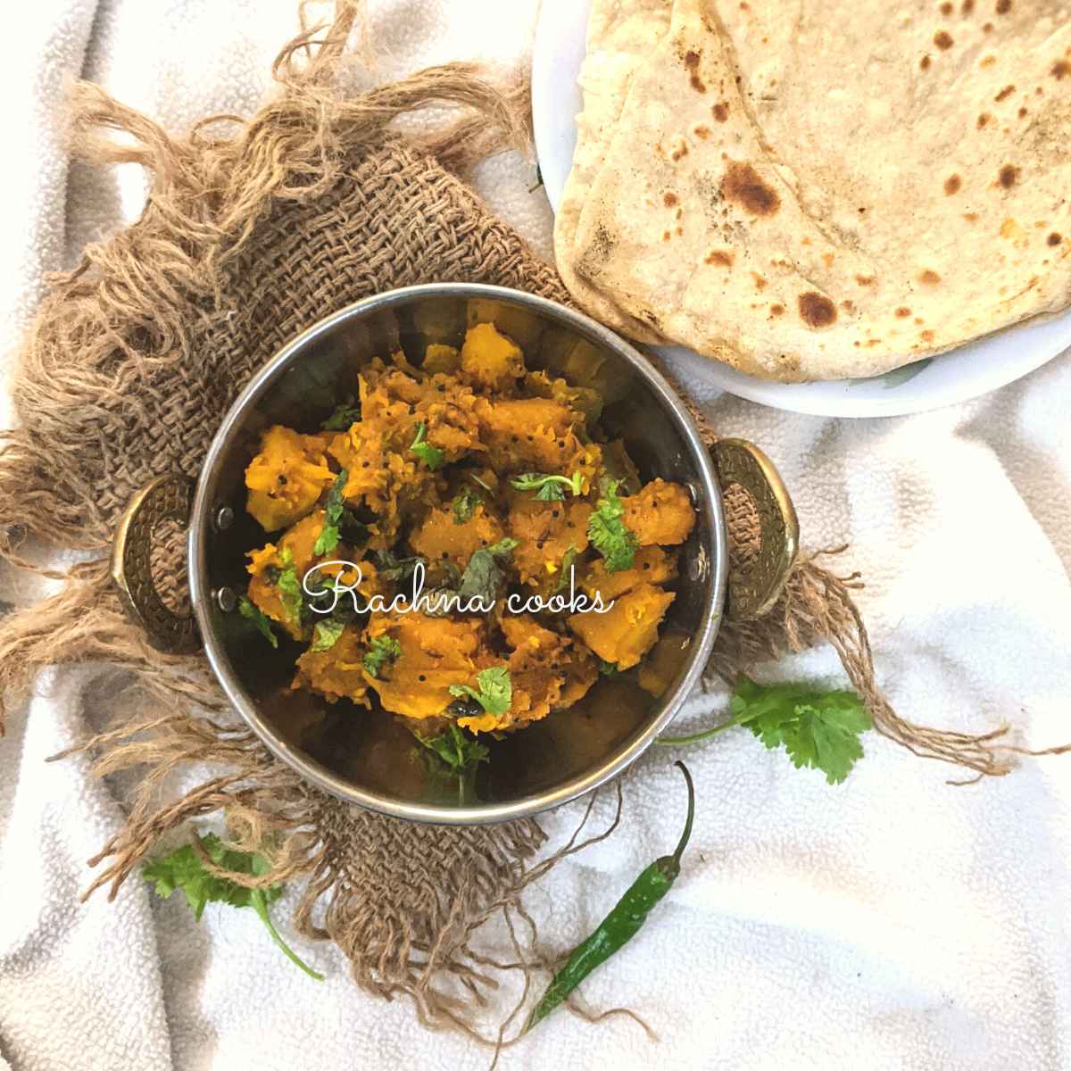 Pumpkin curry in a wok served with a garnish of cilantro with wholewheat parathas in the background.
