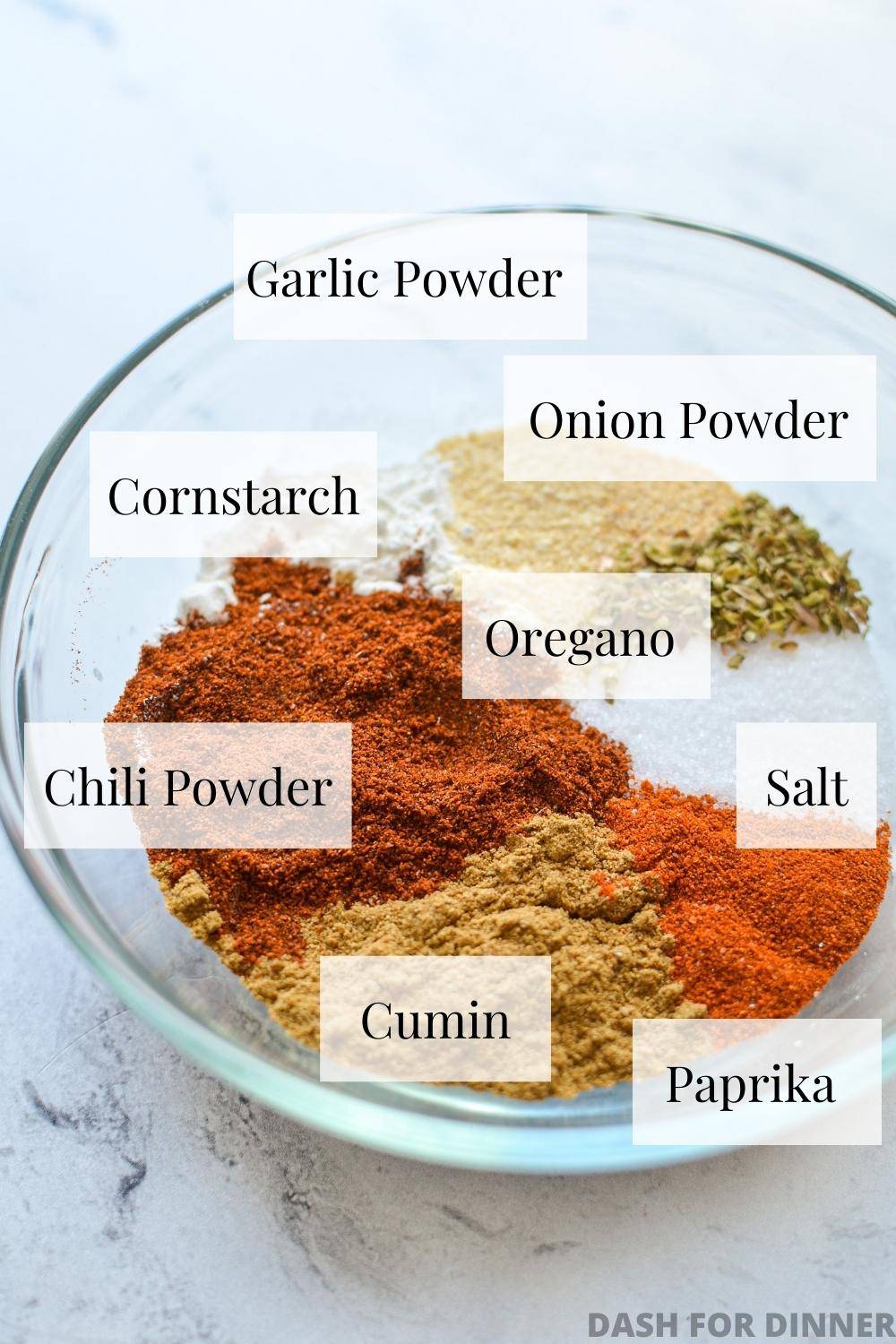 A bowl with various seasonings, labeled, that come together to make taco seasoning.