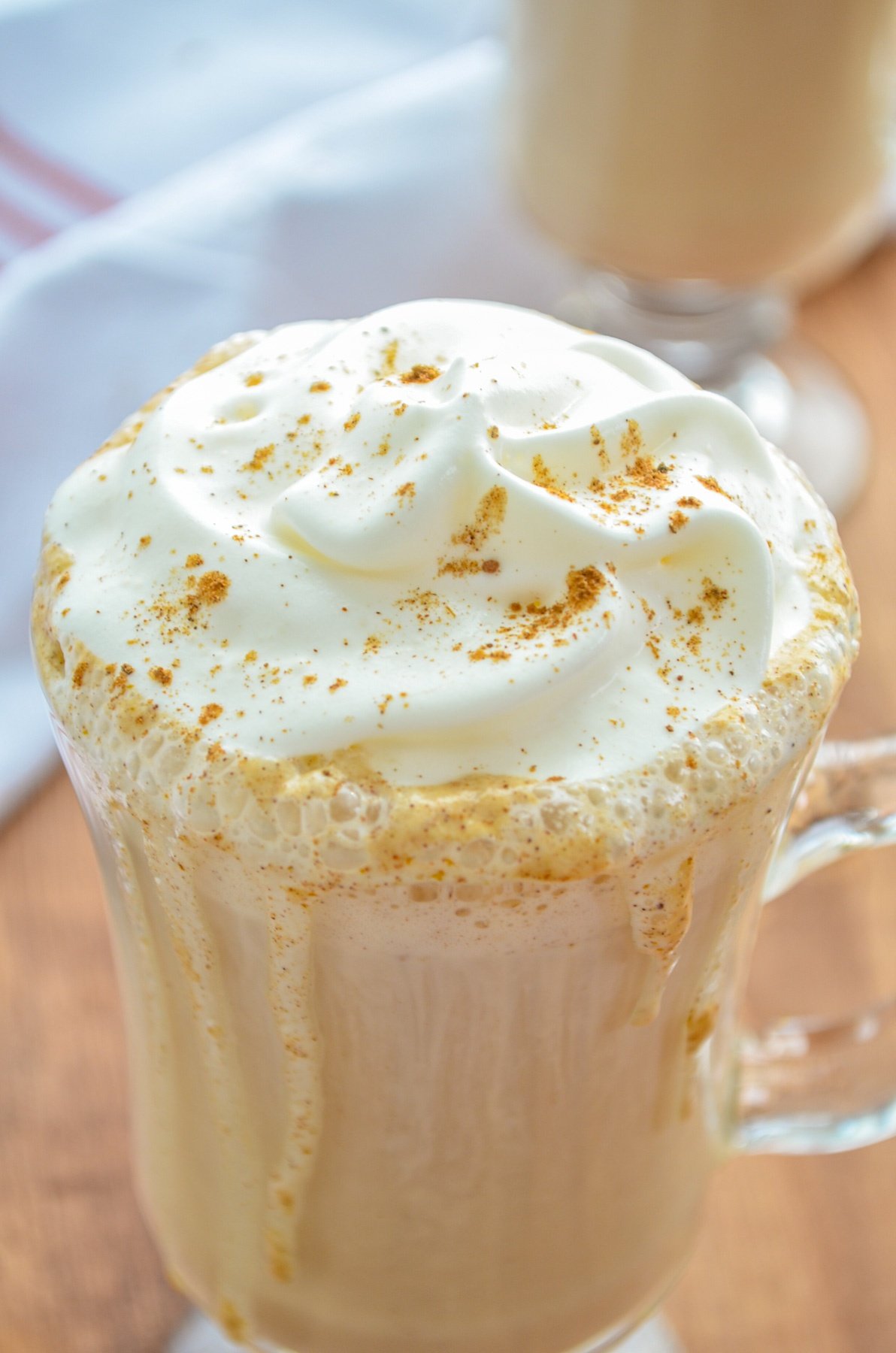 A glass mug of pumpkin spice latte, served with whipped cream and a pinch of pumpkin spice on top.