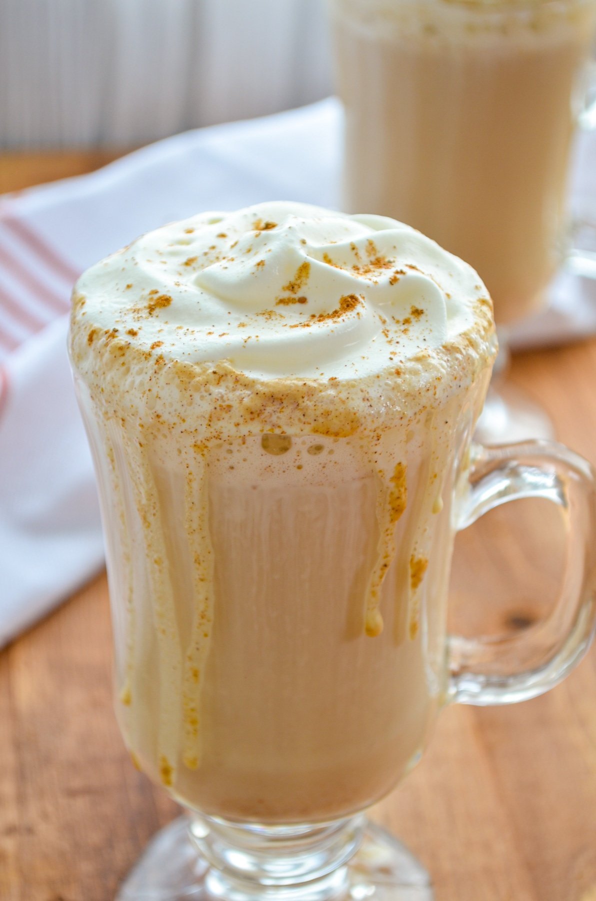 Two glass mugs of pumpkin spice latte, topped with whipped cream.