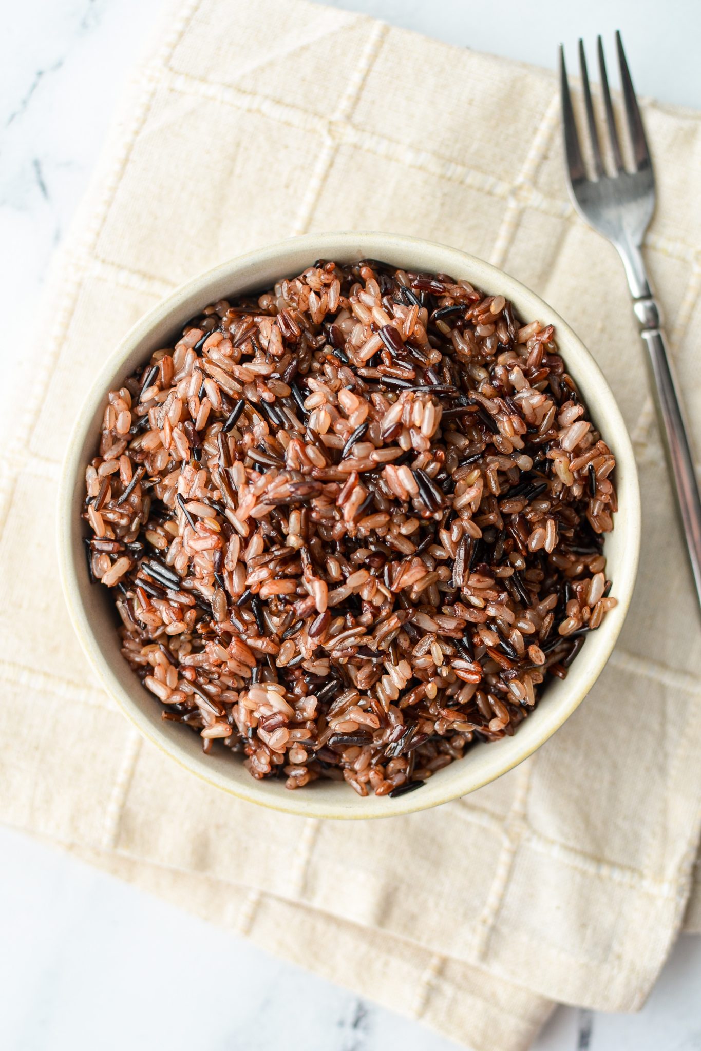 A bowl of wild rice on an off white cloth.