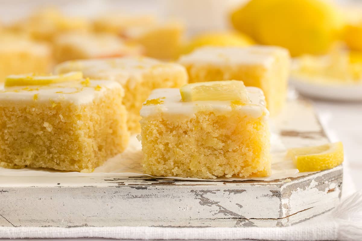 Lemon brownies with white icing and lemon slices on top, arranged on a rustic white wooden surface.