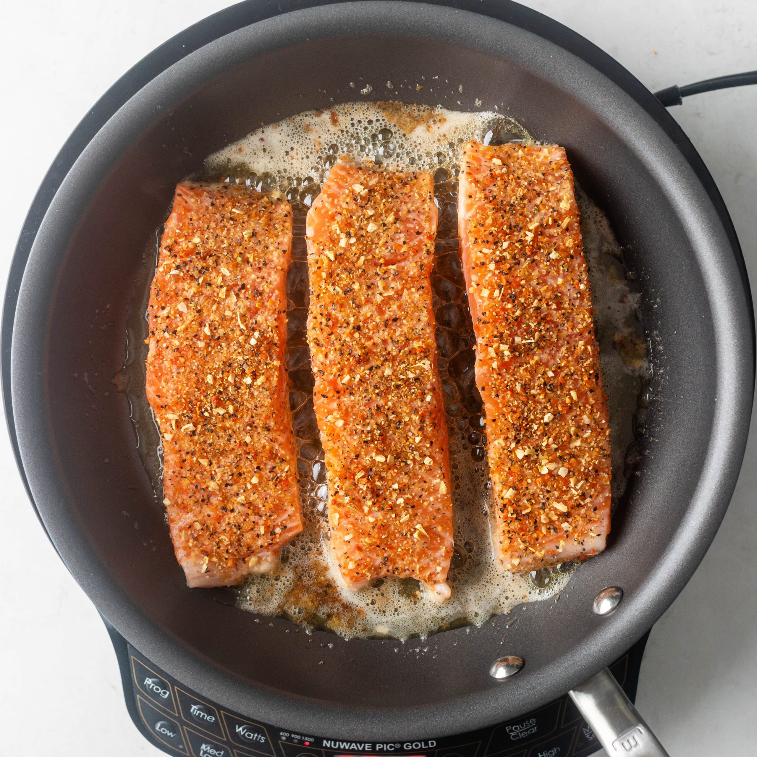 Cooking 3 pieces of lemon pepper salmon in a pan with butter and olive oil. 