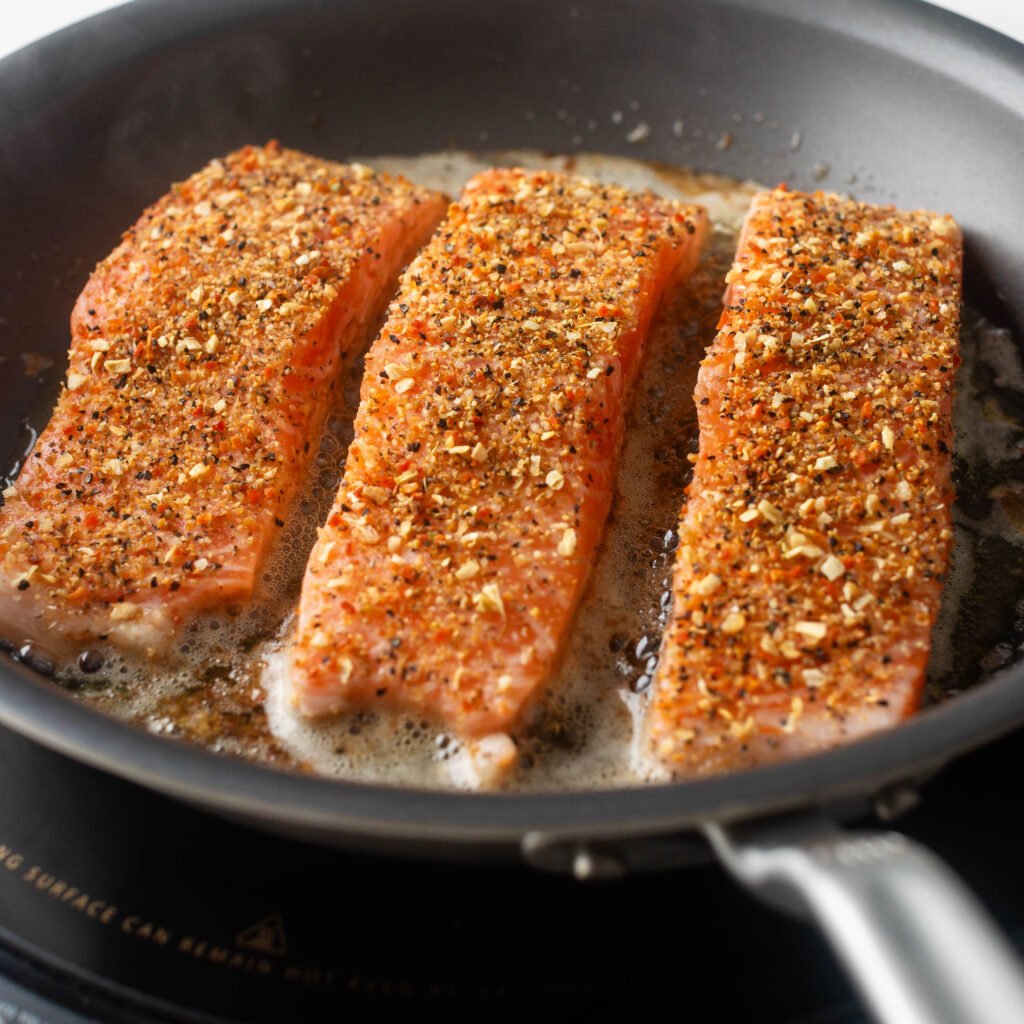 Cooking the seasoned salmon until the skin is crispy. 