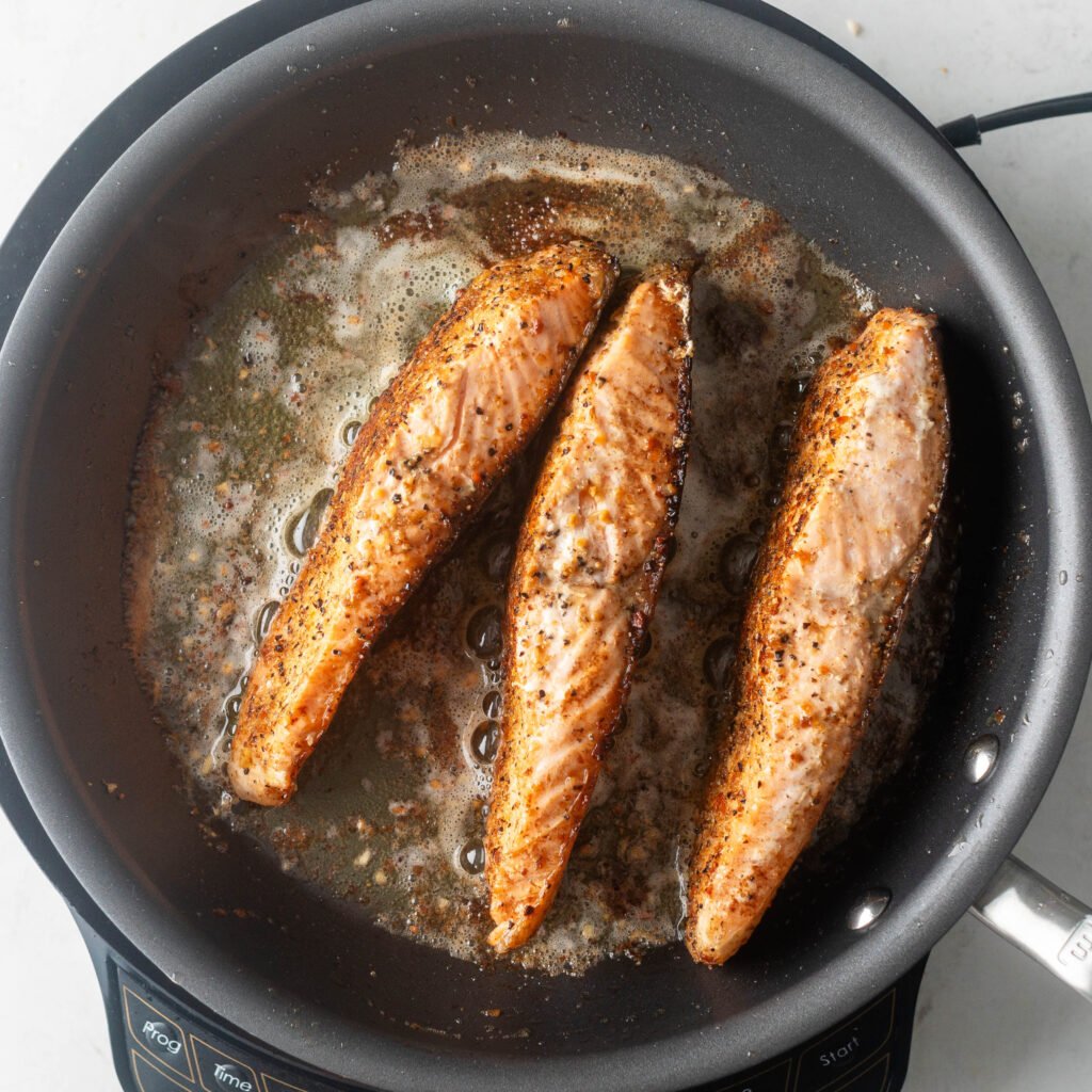 Cooking 3 pieces of lemon pepper salmon on their sides in butter and olive oil. 