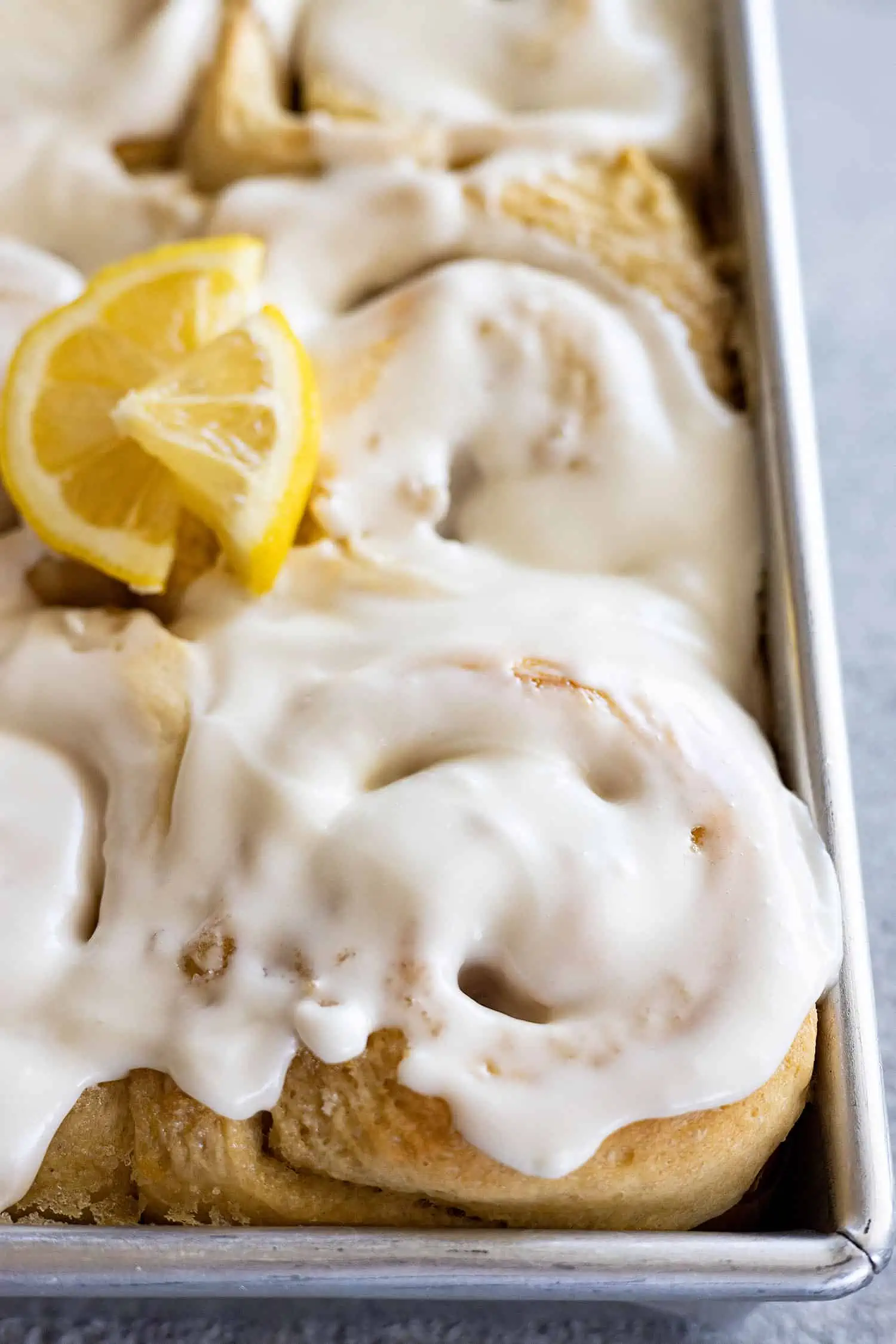 Close up of lemon sweet rolls in a pan topped with cream cheese frosting.