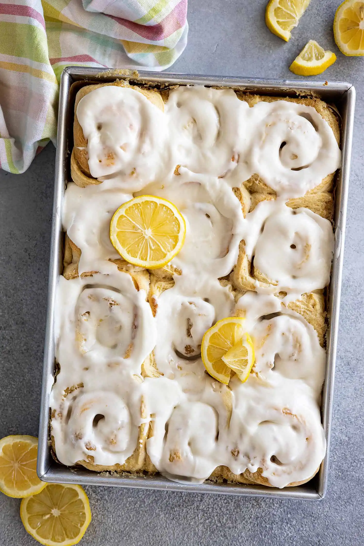 Overhead view of a pan of lemon sweet rolls topped with a cream cheese frosting and garnished with a few lemon slices.