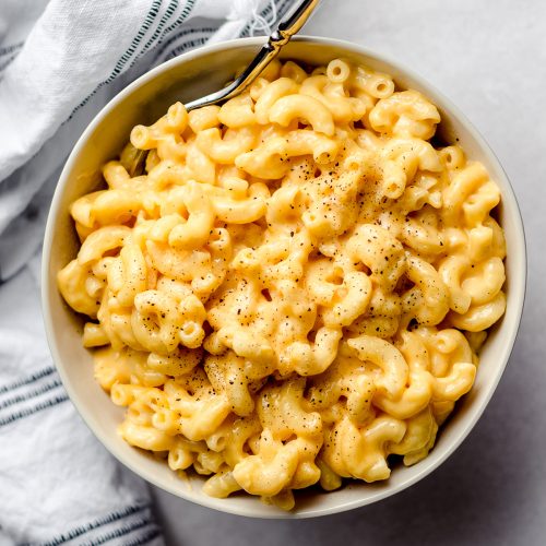 A bowl of macaroni and cheese, with a fork stuck into the side.