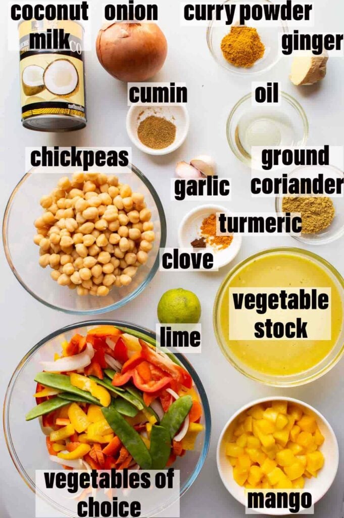 top down view of labelled ingredients including: coconut milk, onion, curry powder, ginger, ground coriander, garlic, cumin, chickpeas, turmeric, clove, vegetable stock, lime, vegetables of choice and mango.