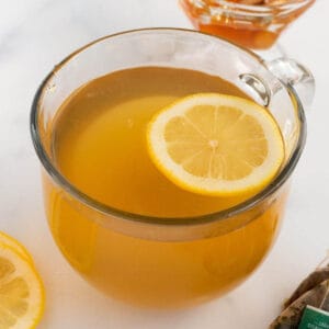 A clear coffee mug with an amber tea and lime slice on top.