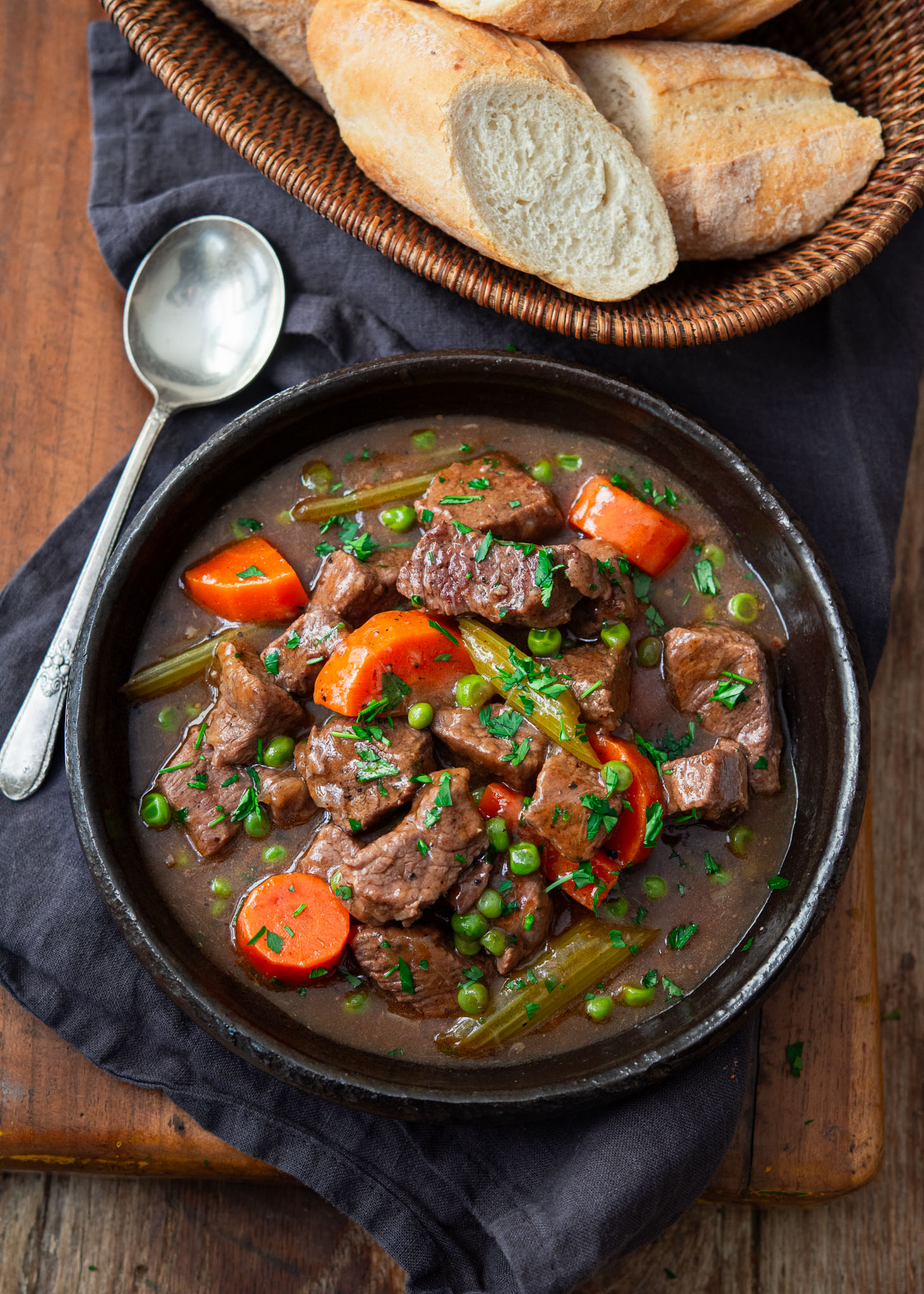 Old time beef stew in a serving bowl with crusty bread on the side.