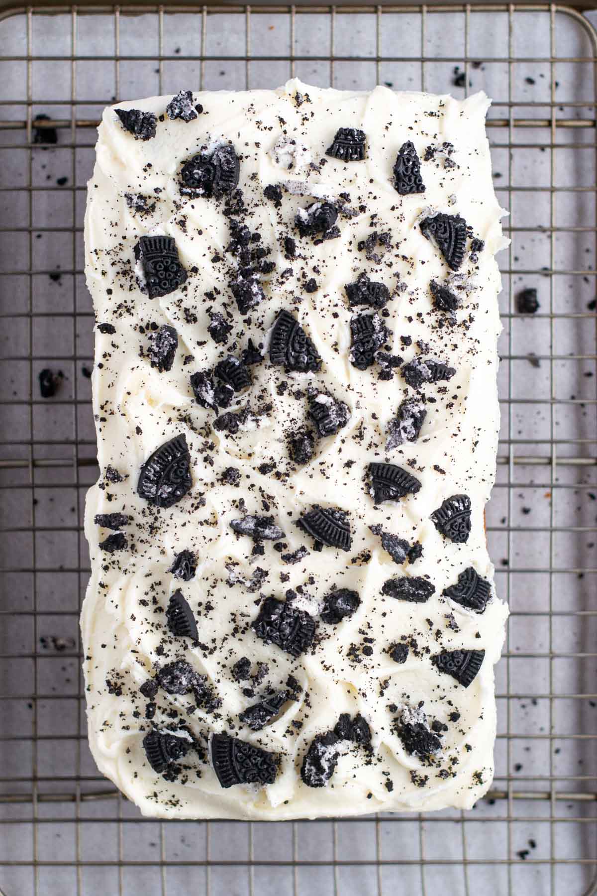 cake on a cooling rack with cookie pieces on vanilla cream icing