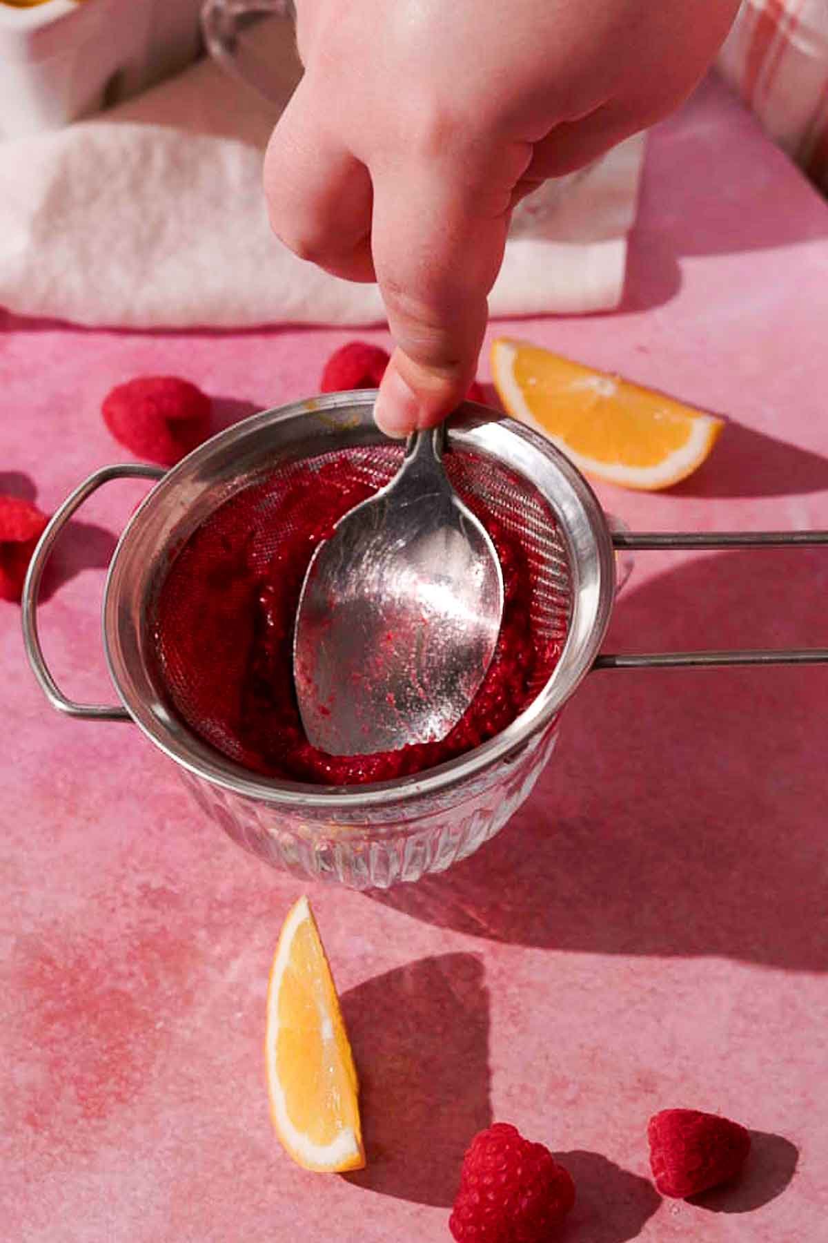 straining raspberries through a metal sieve 