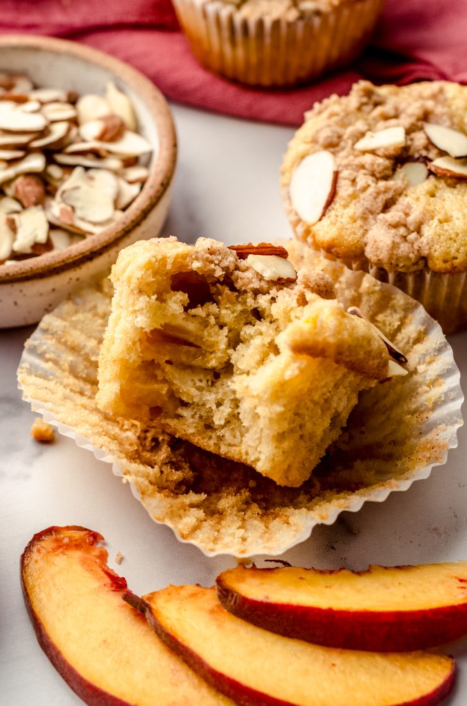 A photo of a peach almond streusel muffin with a bite taken out of it.
