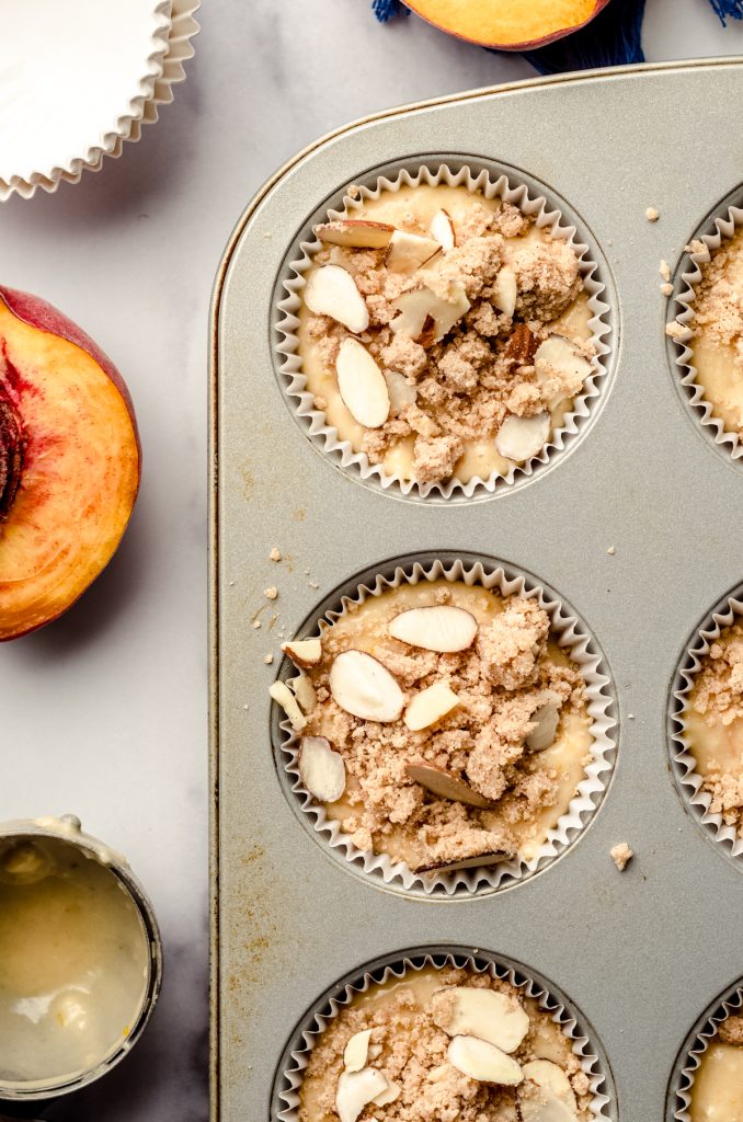Peach almond streusel muffin batter in a cupcake pan ready to bake.